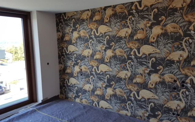Innenraum mit Fenster und Wand mit Tapete in dunklem Hintergrund und goldenem Flamingo-Motiv in verschiedenen Positionen.
