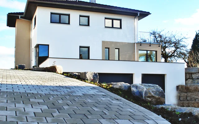 Moderner zweistöckiger Wohnhauses mit weißer Fassade und großer gepflasterter Auffahrt unter blauem Himmel.