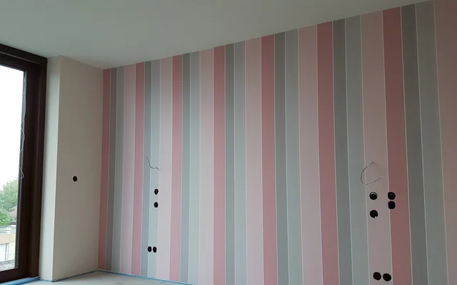 Wand mit vertikalen Streifen in Rosa-, Grau- und Weißtönen, daneben ein großes Fenster mit Blick nach draußen.