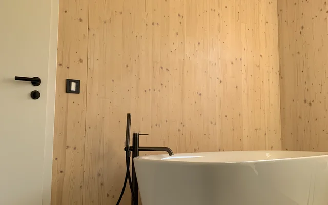 Moderner Wellness-Badezimmerbereich mit freistehender weißer Badewanne vor einer Wand und Decke aus hellem Holz.