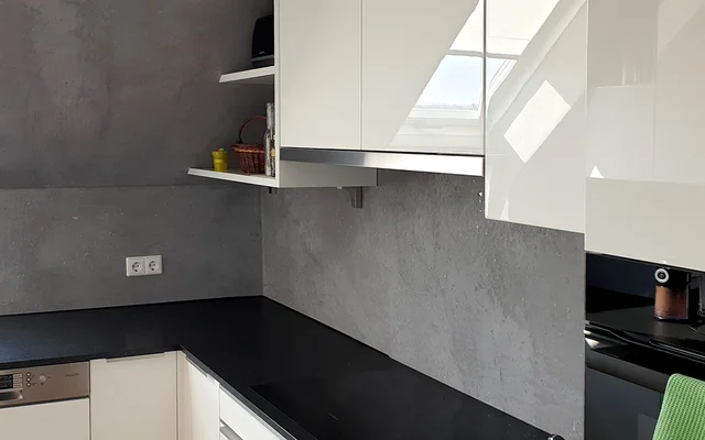 Moderner Küchenarbeitsplatz mit mattem schwarzen Arbeitsplatten und weißen, glänzenden Oberschränken vor einer grauen Wand.