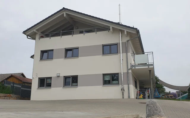 Modernes zweistöckiges Wohnhaus mit hellgrauer Fassade und dunklen Fensterrahmen an bewölktem Tag.